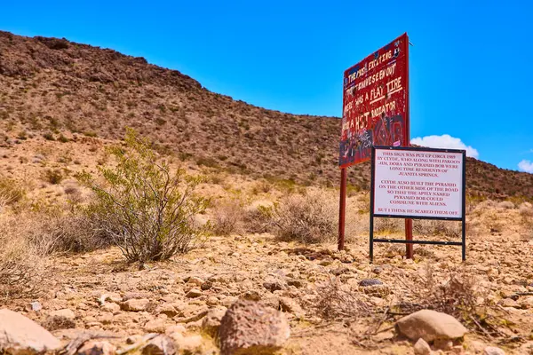 Yıpranmış tabela ve engebeli kayalar Amerika Birleşik Devletleri 'nde açık mavi gökyüzü altında seyrek Nevada bitki örtüsü bulunan Altın Butte Ulusal Anıtı çölünün ortasında göze çarpıyor.