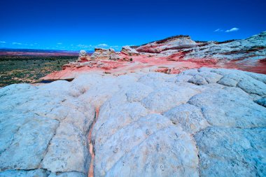 Beyaz kaya oluşumları, Ak Kol 'da, Vermilion Uçurumları Ulusal Anıtı' nda, Arizona Mermer Kanyonu 'ndaki derin mavi gökyüzünün altında canlı kırmızı kumtaşı katmanlarının üzerinde yükselir.