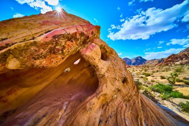 Kum taşı kavisli oluşum, parlak güneşin altında parıldıyor. Nevada 'daki Altın Kalça Ulusal Anıtı' nda. Engebeli dağlar ve çöl bitkileri canlı mavi gökyüzünün altında uzanıyor.