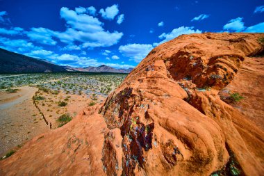 Kızıl kumtaşı kayaları, Nevada 'daki Gold Butte Ulusal Anıtı' nda canlı bir gökyüzünün altında uzanan çöl bitki örtüsü ve uzak dağlarla ön plana hükmediyor.