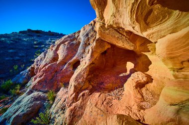 Güneş ışığı alan kumtaşı mağarası ve yıpranmış kaya oluşumları Gold Butte Ulusal Anıtı Nevada 'nın kurak yamaçlarından yükseldi parlak mavi gökyüzünün altında