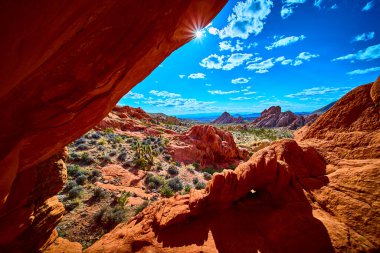 Güneş ışığı, doğal bir kemer düzeninden geçer. Kırmızı kayalar çöl bitkilerini ve Whitney Pocket Nevada yakınlarındaki Gold Butte Ulusal Anıtı 'nın geniş manzarasını vurgular.