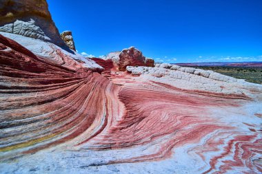 Parlak kumtaşı dalgaları Vermilion Cliffs Ulusal Anıtı Arizona 'da Amerikan Güneybatısı' nın ruhunu yakalayan açık mavi gökyüzü altında koyu kırmızı ve pembe çizgilerle beyaz cebi silip süpürüyor.