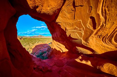 Nevada 'daki Whitney Pocket Ulusal Anıtı' nda kırmızı kaya kemeri oluşumu geniş bir çöl manzarasını ve parlak mavi gökyüzünün altındaki uzak dağları çerçeveler.