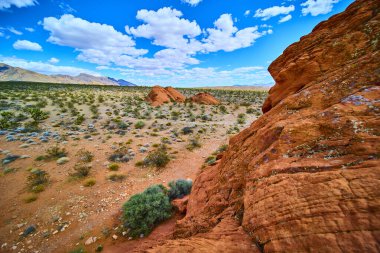 Canlı kırmızı kumtaşı kayaları, yerli bitkiler ve Nevada Ulusal Anıtı 'ndaki uzak dağlarla dolu bir çöl arazisinin üzerinde yükseliyor. Doğal bir merak ve açık alan hissi yaratıyor.