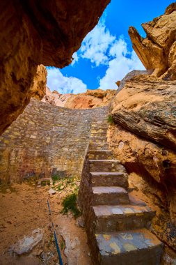 Nevada Ulusal Anıtı 'nın Whitney Cep Bölgesi' nde engebeli kumtaşı ve mavi bir gökyüzünün altında eğri bir sarnıç duvarının yanında yükselen taş adımlar.