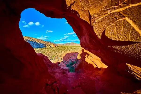 Canlı kırmızı kaya kemeri oluşumu Nevada çöl manzarasını çerçeveliyor. Whitney Pocket yakınlarındaki Gold Butte Ulusal Anıtı 'ndaki mağara duvarına bir insan gölgesi uzanıyor.