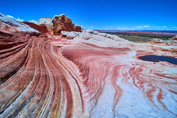 Parlak mavi gökyüzü altında Vermilion Cliffs Ulusal Anıtı Arizona 'daki White Pocket' da kıvrımlı kum taşı desenleri ve katmanlı kaya oluşumları çarpıcı bir çöl manzarası oluşturur.