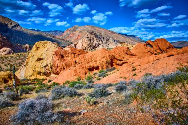 Altın Butte Ulusal Anıtı 'nda Nevada çölünden dramatik kumtaşı oluşumları yükseliyor. Whitney Pocket yakınlarında engebeli dağlar ve çöl bitkileri parlak mavi gökyüzünün altında.