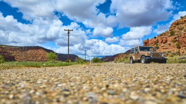 Bir bronz Jeep Wrangler, Kanab Utah 'ta dramatik kırmızı kaya oluşumları ve süpüren bulutlar tarafından çerçevelenmiş engebeli bir çöl yolunda duruyor. Macera seyahati ve açık yolların özgürlüğü için mükemmel bir tema..