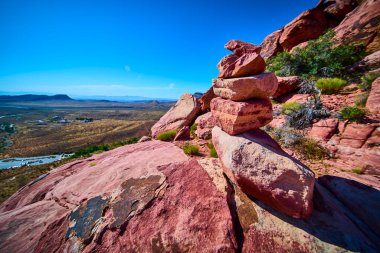Las Vegas Nevada yakınlarındaki Red Rock 'ta açık mavi gökyüzünün altındaki geniş bir çöl vadisine bakan dengeli bir kaya yığını veya cairn üzerinde durmaktadır..