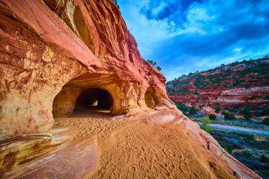 Altın saat güneş ışığı Kanab Utah yakınlarındaki kırmızı kumtaşı mağaraları aydınlatırken engebeli kanyonlar ve dolambaçlı bir yol dramatik güneybatı manzarasını keşfetmeye davet ediyor.