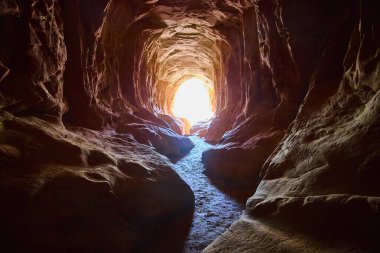 Güneş ışığı Kanab Utah yakınlarındaki Ejderha Mağarası 'na akıyor. Kum taşından örülmüş duvarları vurguluyor. Macera araştırmalarına davetiye çıkaran dolambaçlı bir yol.
