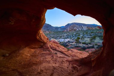 Kırmızı bir kaya kemeri oluşumunun içinden çöl arazisine ve engebeli dağlara bakarken Gold Butte Ulusal Anıtı Nevada 'daki Whitney Pocket' e bakın.