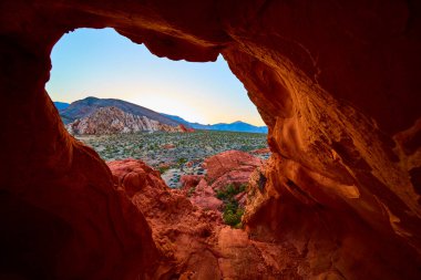 Nevada 'daki Whitney Pocket Ulusal Anıtı' nda kırmızı kaya kemeri oluşumu gündoğumunda çöl ve uzak dağları çerçeveler ve canlı jeoloji ve huzurlu atmosferi yakalar.