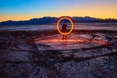 Çelik yün ören bir insan Nevada 'da Boulder City' de kıvılcımlar yaratıyor Nevada 'daki kuru göl yatağında renkli akşam gökyüzüne karşı silueti olan dağlar.