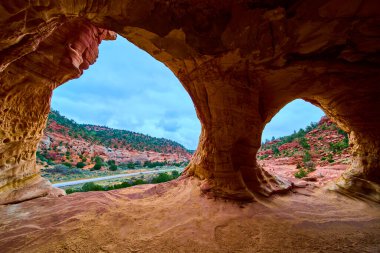 Kanab Utah yakınlarındaki doğal bir kumtaşı mağarasından bakıldığında geniş kırmızı kaya oluşumları, eşsiz erozyon şekilleri ve Amerika 'nın manzaralı çöl manzarası boyunca uzanan dolambaçlı bir yol görülüyor.
