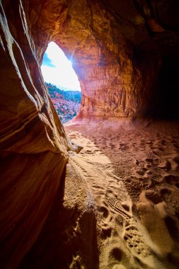 Günışığı Utah 'taki Kanab kumtaşı mağarasına akar ve kırmızı kaya duvarlarını işaretler, kumlu zeminler ve macera ve keşif için mükemmel bir çöl manzarası oluşturur.