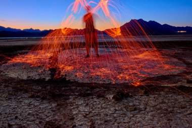 Siluetli bir figür Nevada 'daki Boulder City' de çelik yün örüyor Nevada 'daki kuru göl yatağında altın saat gökyüzü ve dağlar altında kıvılcımlar uçuşuyor.
