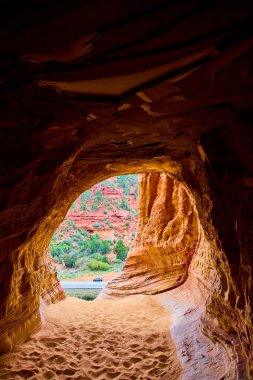 Utah 'taki Kanab kum mağarasının içinden bakıldığında güneşli bir çöl yolu, kırmızı kumtaşı duvarlar ve Amerikan güneybatısındaki macera ve keşif ruhunu yansıtan manzaralı bir uçurum görünüyor.