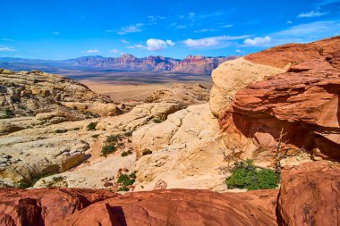 Canlı kırmızı ve kremalı Calico kayaları Las Vegas yakınlarındaki Kızıl Kaya Kanyonu 'na bakar. Uzak dağlar ve açık mavi gökyüzü doğal bir merak hissi yaratır..
