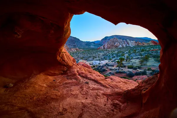 Kırmızı bir kaya kemeri oluşumunun içinden çöl arazisine ve engebeli dağlara bakarken Gold Butte Ulusal Anıtı Nevada 'daki Whitney Pocket' e bakın.