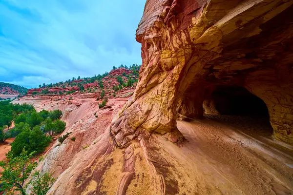 Güneş ışığı Kanab Utah 'taki bir kumtaşı mağarasının kemerli girişinden geçer çizgili kırmızı kaya duvarlarını vurgular ve bir macera ve ekolojik seyahat için çöl manzaralarını süpürür.