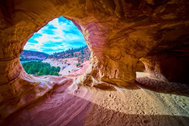 Kanab Utah yakınlarındaki bir kumtaşı mağarasının içinden bakıldığında dramatik kırmızı kaya oluşumları ve Amerika 'nın güneybatı çölünde yemyeşil bir vadi ortaya çıkıyor.