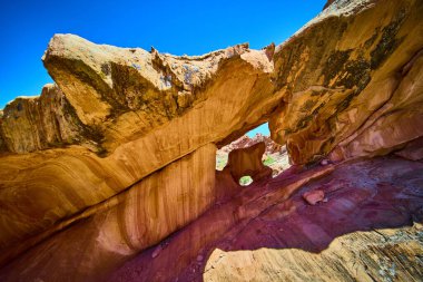 Güneşli kumtaşı kemeri ve katmanlı kaya dokusu, açık mavi gökyüzünün altındaki Nevada 'daki Whitney Pocket Ulusal Anıtı' nda nadir bulunan bir kemerin çerçevesini oluşturuyor.