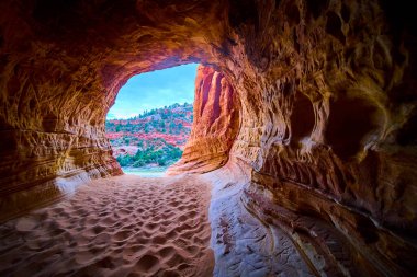 Altın saat ışığı Kanab Utah yakınlarındaki bir kumtaşı mağarasına akar. Kızıl kaya oluşumları ve açık mavi gökyüzü ile nefes kesici bir çöl manzarası çerçeveler. Macera ve keşif için mükemmel bir manzara.