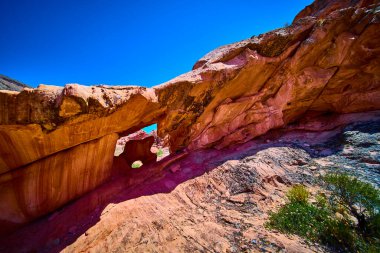 Doğal bir kemer oluşumunun çarpıcı görüntüsü ve Nevada 'daki Gold Butte Ulusal Anıtı' nda Whitney Pocket yakınlarındaki engebeli bir çöl kayasıyla çevrili parlak mavi gökyüzünün altında.