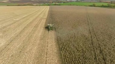 Bir dron mısırları hasat etmek için bir aracın arkasında yükseğe uçar ve yetişir. Kamera birleşimi ortaya çıkarmak için eğilir, sonra öne doğru yükselir ve manzarayı gözler önüne serer..