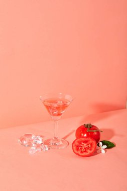 Pembe arka planda bir kokteyl bardağıyla sergilenen taze domatesler. Domates, A ve C vitaminlerinin büyük bir kaynağıdır. Gece körlüğünü önler ve görme yetisini artırır..