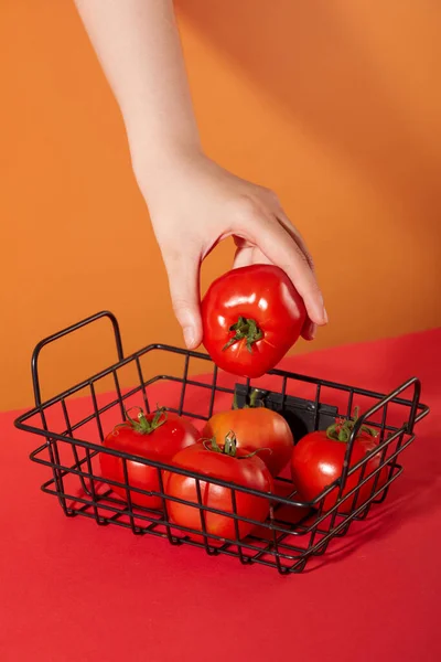 メッシュバスケットにジューシーな赤いトマトを保持しています オレンジと赤の背景 トマトは健康的な食べ物であるだけでなく 肌を美化するために多くの人々によって使用されます — ストック写真