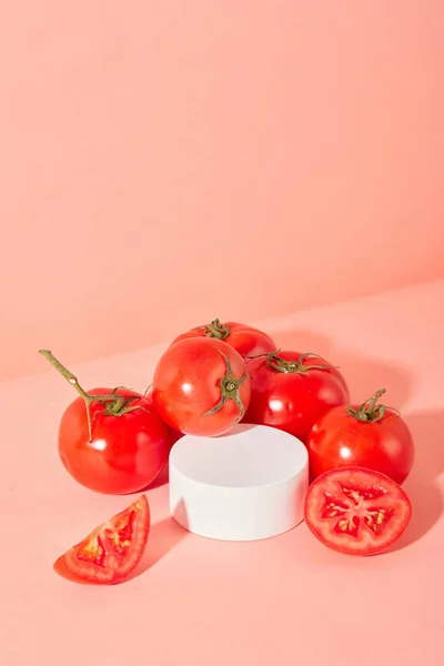 ジューシーな赤いトマトは ピンクの背景に丸いプラットフォームの周りに配置されています トマトエキスで天然化粧品を展示するのに最適なスペースです クローズアップ — ストック写真