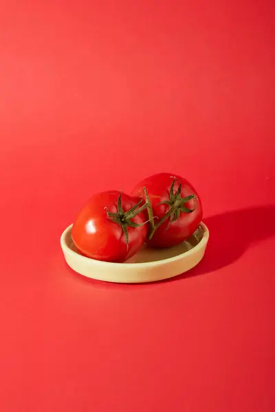 2つのジューシーな赤いトマトは 赤い背景にセラミック皿の上に置かれています トマトは甘くて酸っぱい味があり クールな特性があり エネルギーを作り出し ミネラルを補充する効果があります — ストック写真