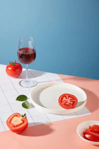 新鮮なトマト ホワイトセラミックプレート 赤ワイングラスがテーブルの上に置かれています ブルーとピンクの背景 トマトのビタミンCは 皮膚の弾力性を改善するためにコラーゲンの生産を刺激するのに役立ちます — ストック写真