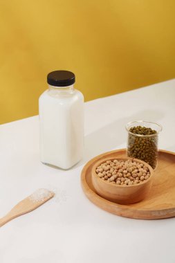 Soya fasulyesi dolu ahşap kase ve tepsiye konmuş yeşil fasulye şişesi. Etiketsiz süt şişesi sergileniyor. Organik içecek ürünleri için minimalist modelleme