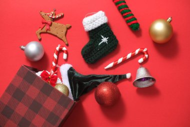 Kırmızı arka planda, Noel süslemeleri için kullanılan sevimli nesneler küçük bir hediye kutusundan düşüyor. Her yıl 25 Aralık 'ta kutlanan Mutlu Noeller sembolü.