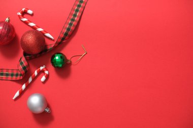 Kırmızı arkaplan ve yeni yıl kartı için boş alan. Renkli mücevherler, baston şekerler ve kurdeleler. Tasarım için yaratıcı fikirler