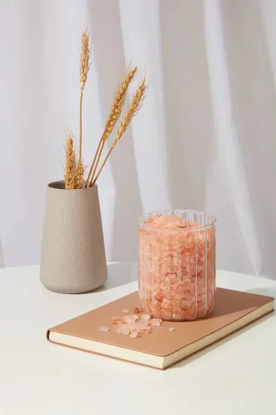 ノートに置かれたピンクのヒマラヤ塩を多く含む瓶は 花の鍋で展示されています 白いカーテンが飾られています ヒマラヤ塩は 最も敏感な皮膚タイプでも恩恵を受けることができます — ストック写真
