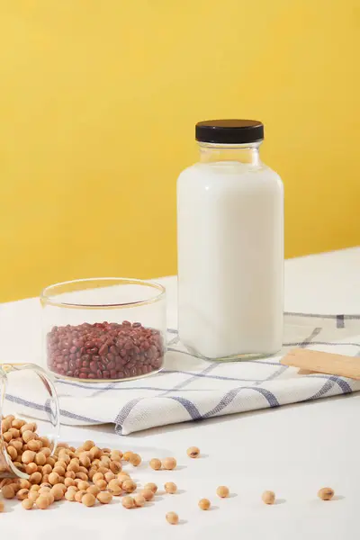Fresh milk bottle with empty label placed on a fabric next to a bowl of red beans. Many soybeans displayed. Beans are high in beneficial fiber provides many health benefits