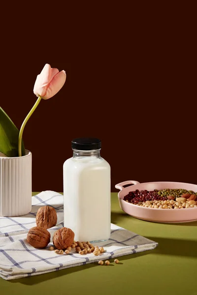 生的混合坚果被陈列在一个粉红色的盘子里 一个没有标签的牛奶瓶 上面有核桃和大豆 有机饮料的概念 — 图库照片