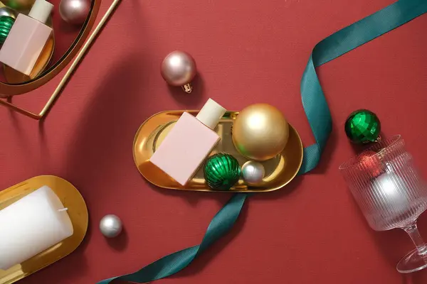 クリスマスコンセプトの広告やブランディング製品のシーン 装飾が施された金色のトレイに置かれたピンクの化粧品ボトル 赤い背景にバブル リボン ろうそく — ストック写真