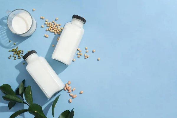 Two blank label bottles and a glass cup filled with milk displayed with green beans, soybeans and peanuts. Copy space. Concept of organic foods advertising