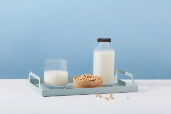 Empty label milk bottle arranged on a tray in pastel color with a cup of milk and wooden bowl of soybeans. Template for mockup your design