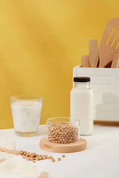 木製の表彰台に置かれた大豆の透明なボウルは 牛乳のカップとボトルが表示されます フロントビュー 大豆ミルクのタンパク質は健康的です — ストック写真