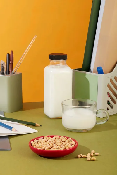 Blank label bottle of milk displayed on an office desk with a milk cup and a red dish of soybeans. Organic product advertising with empty label