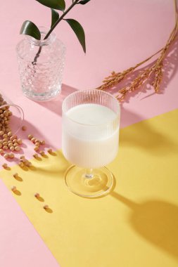 Pembe ve sarı yüzeye bir bardak soya sütü ve bir kap yeşil yaprak. Soya sütü protein ve B vitaminleriyle sağlıklı enerji seviyelerini arttırır