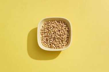 Sarı arka planda bir sürü soya fasulyesiyle dolu seramik bir kasenin üstünden görüntü. Soya ve soya yemekleri özellikle vejetaryen ve vejetaryen diyetleri takip edenler için popülerdir.